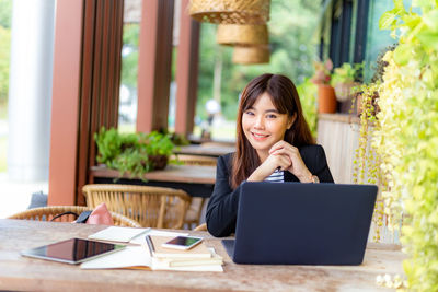 Portrait of young woman using phone while sitting on table