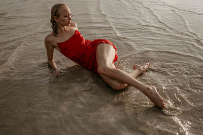 A young girl in a red dress lies in sea water