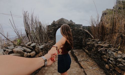 Cropped image of woman holding friend hands on fort against sky