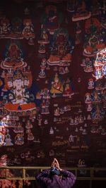 Rear view of man praying against mural in buddhist temple