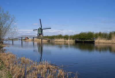 Traditional windmill by lake against sky
