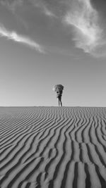 Girl with umbrella standing at desert against sky