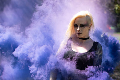 Portrait of young woman with make-up standing amidst smoke