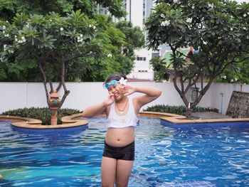 Woman gesturing peace sign in swimming pool against trees