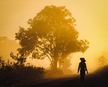 Silhouette man riding bicycle on field against sky during sunset