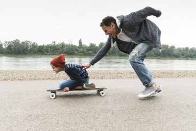 Happy father pushing son on skateboard at the riverside