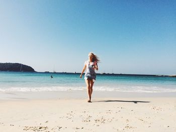 Full length of young woman walking at beach against clear sky