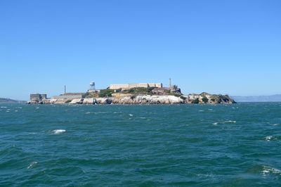 Buildings by sea against clear blue sky