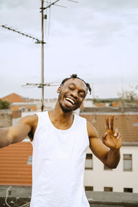 Cheerful young man with eyes closed gesturing peace sign