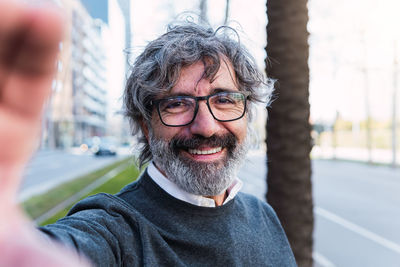 Happy mature caucasian man taking a selfie portrait at the street. smiling at the camera
