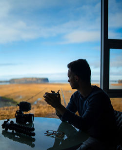 Side view of young man looking through window while sitting in restaurant