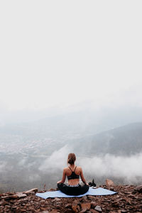 Woman sitting on mountain against sky