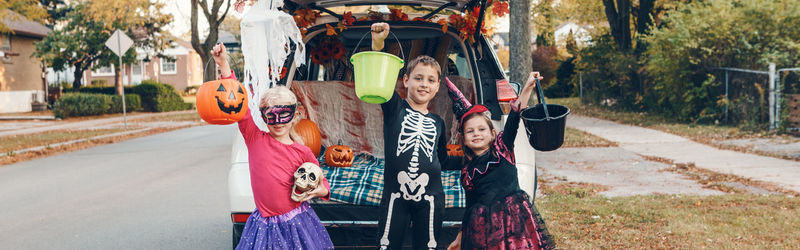 Portrait of smiling kids standing by car trunk