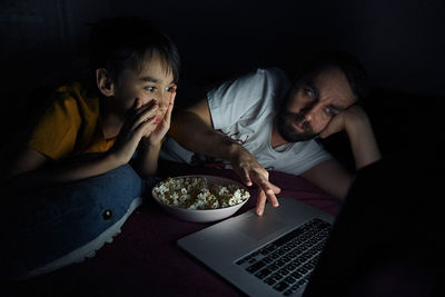 High angle view of boy with father watching movie in darkroom