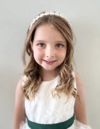 Portrait of young girl in a flower girl dress standing against wall