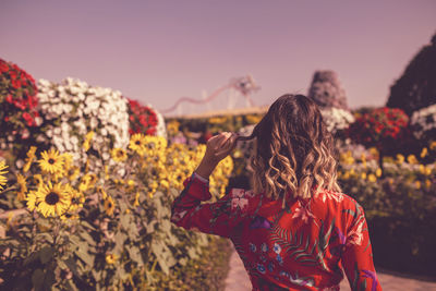 Rear view of woman standing on red flowering plant against sky