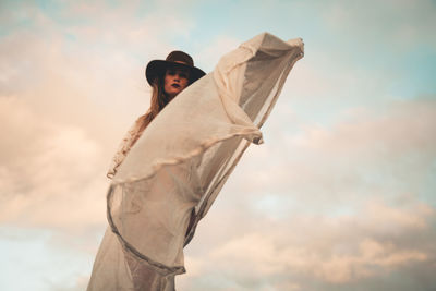 Woman wearing white dress while standing against cloudy sky during sunset