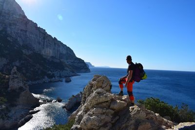 Side view of male hiker standing on cliff against sea