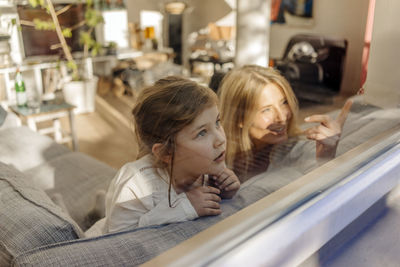 Mature woman and girl at home on couch looking out of window