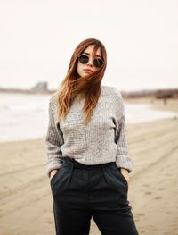 Portrait of young woman standing at beach against clear sky