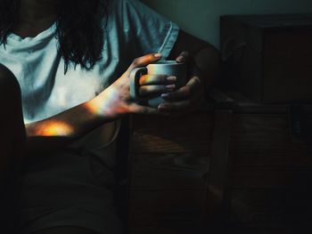 Midsection of woman holding cup while sitting at home