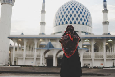 Rear view of young woman standing outside mosque against clear sky