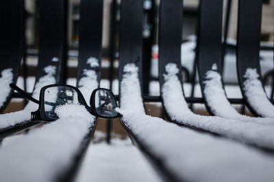 Close-up of a pair of broken reading glasses left on a snowy snow park bench 