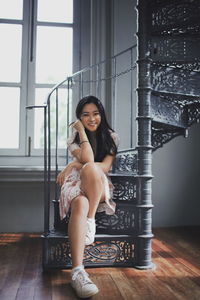 Portrait of smiling young woman sitting on spiral staircase at home