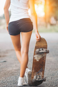 Low section of woman with skateboard standing on road