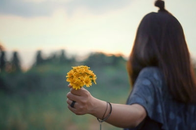 Midsection of woman holding yellow flowering plant during sunset