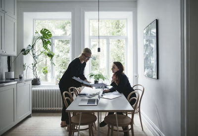 Female colleagues discussing over document at table in home office