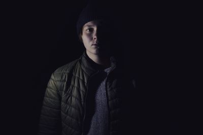 Portrait of man standing against black background