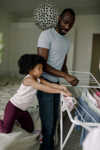 Daughter learning to arrange clothes on drying stand by father at home