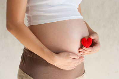 Midsection of pregnant woman holding heart shape against white background
