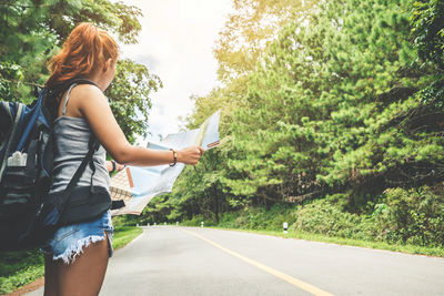 Rear view of woman holding map on road