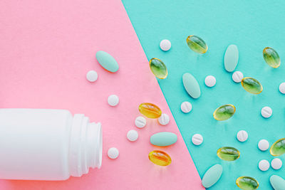 Directly above shot of pills spilling from bottle against pink background