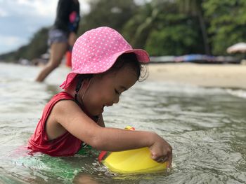 Girl playing with bucket while sitting at beach