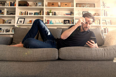 Full length of man using mobile phone while sitting on sofa at home