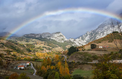 Picturesque autumn landscape of high mountains with low clouds, rainbow and green trees in cantabria