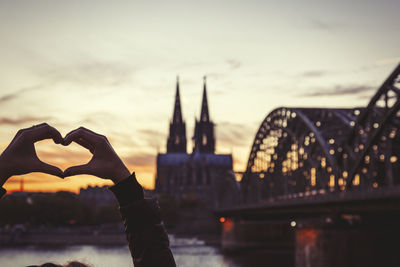 Germany, cologne, woman shaping heart with her hands in front of cologne cathedral and hohenzollern bridge at dusk