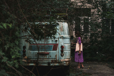 Rear view of woman standing in forest in front of abandoned van