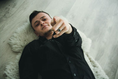 High angle portrait of man pointing while lying on rug