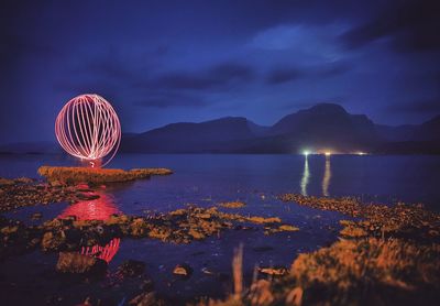 Illuminated beach by sea against sky at night