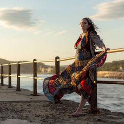 Young woman standing on beach against sky during sunset