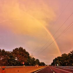 Road by trees against sky during sunset