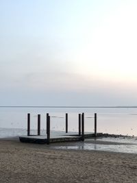 Wooden posts on beach against sky during sunset