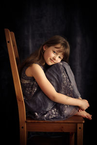 Portrait of cute girl sitting on chair against black background