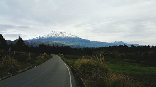 Empty road leading towards mountains against sky