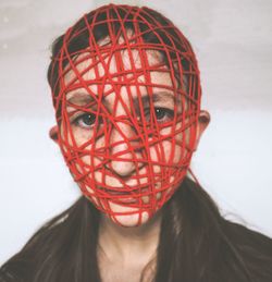 Close-up portrait of young woman with covered face against wall