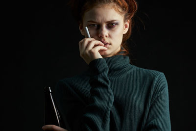 Portrait of young woman holding cigarette against black background